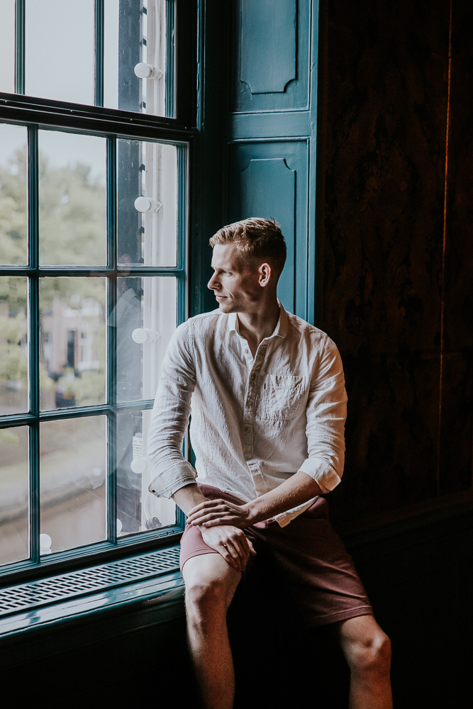 Portret van de bruidegom, in kortebroek, kijkend uit het raam door fotograaf NIckie Fotografie uit Friesland.