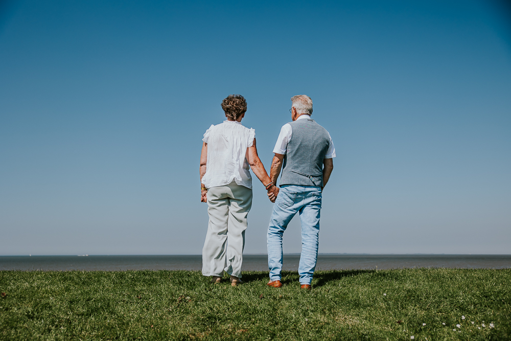 Fotograaf Friesland, Familieshoot Moddergat. Portret van de grootouders, bovenop de zeedijk, terwijl ze over de Waddenzee kijken.