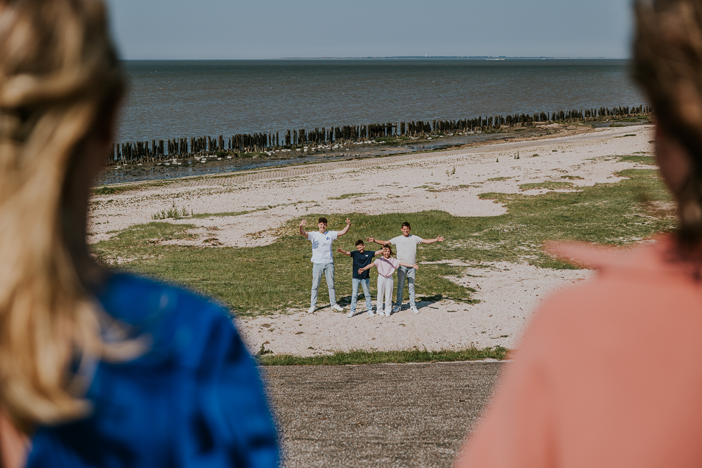 Fotosessie bij de Waddenzee. De kinderen staan, onderaan de dijk, met open armen op hun ouders te wachten. Fotoreportage door fotograaf Nickie Fotografie uit Friesland.