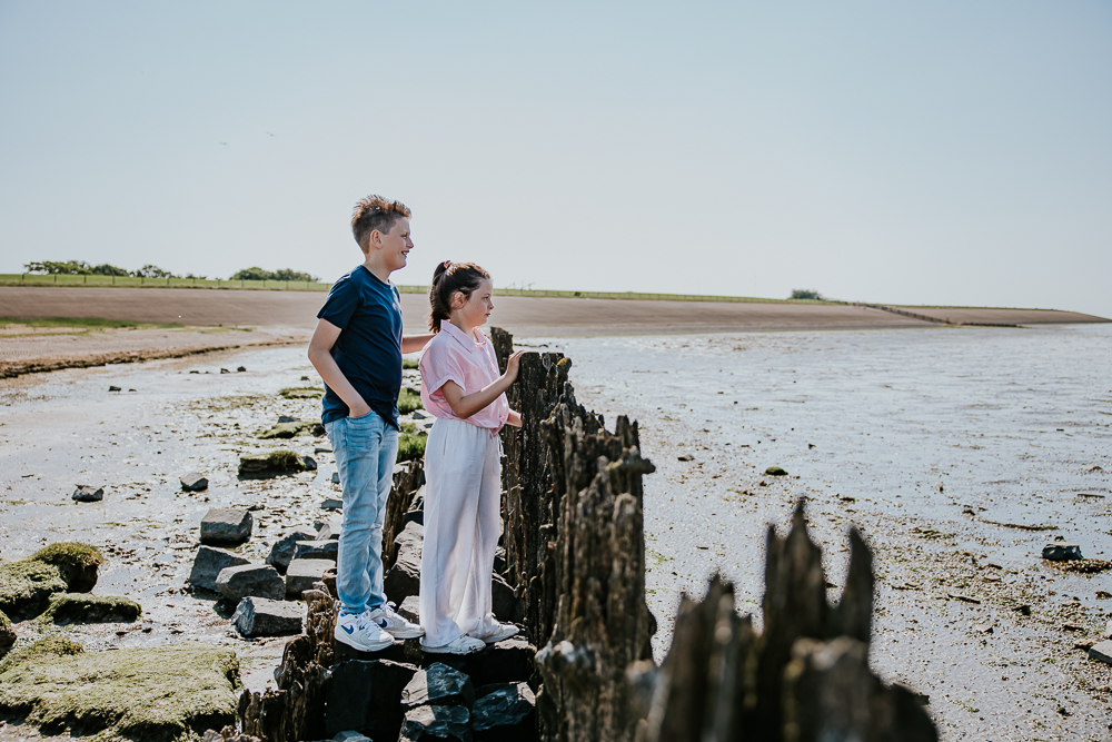 Familieshoot Moddergat. Portret van broer en zus bij de paaltjes, kijkend over de Waddenzee, door portretfotograaf Nickie Fotografie uit Friesland.