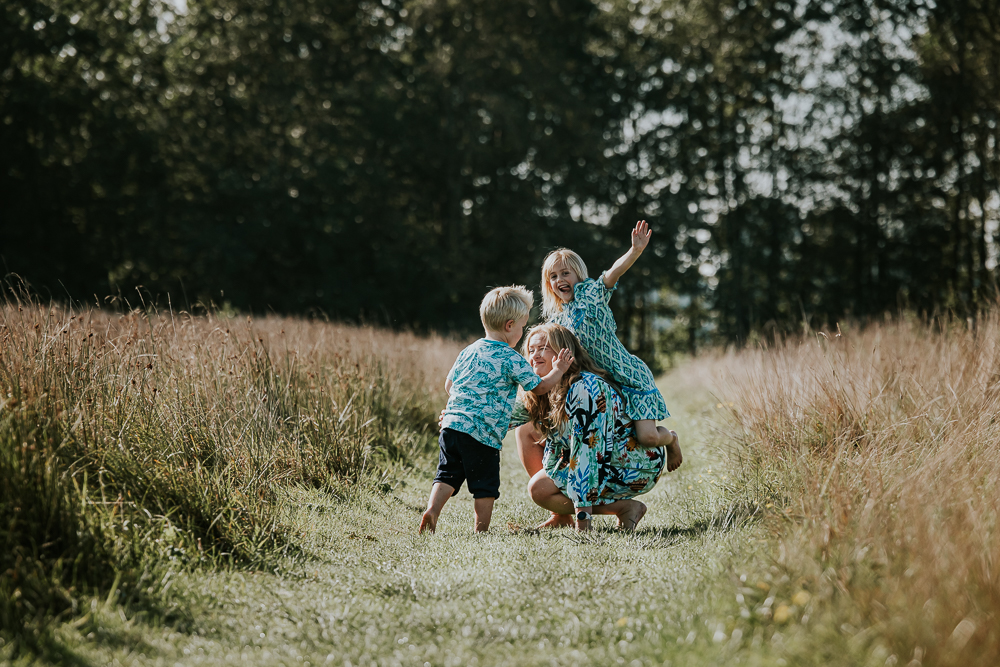 Lifestyle gezinsfotografie in de natuur. Moeder en de twee kinderen zijn aan het stoeien. Fotoshoot door Nickie Fotografie.