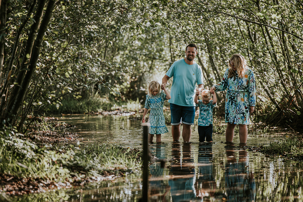 Het gezin loopt door het water en onder de bomen bij het blotevoetenpad van Opende te Groningen. Gezinsfotografie door Nickie Fotografie.