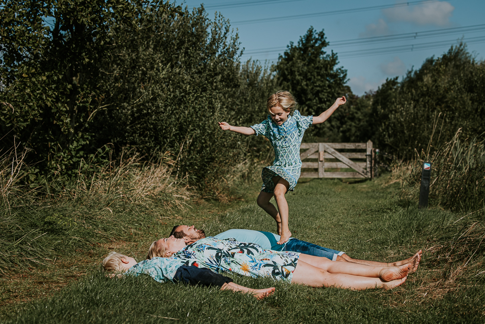 Fotoshoot Groningen. Meisje springt over haar liggende ouders en broertje heen. Lifestyle gezinsfotoreportage door fotograaf Nickie Fotografie.