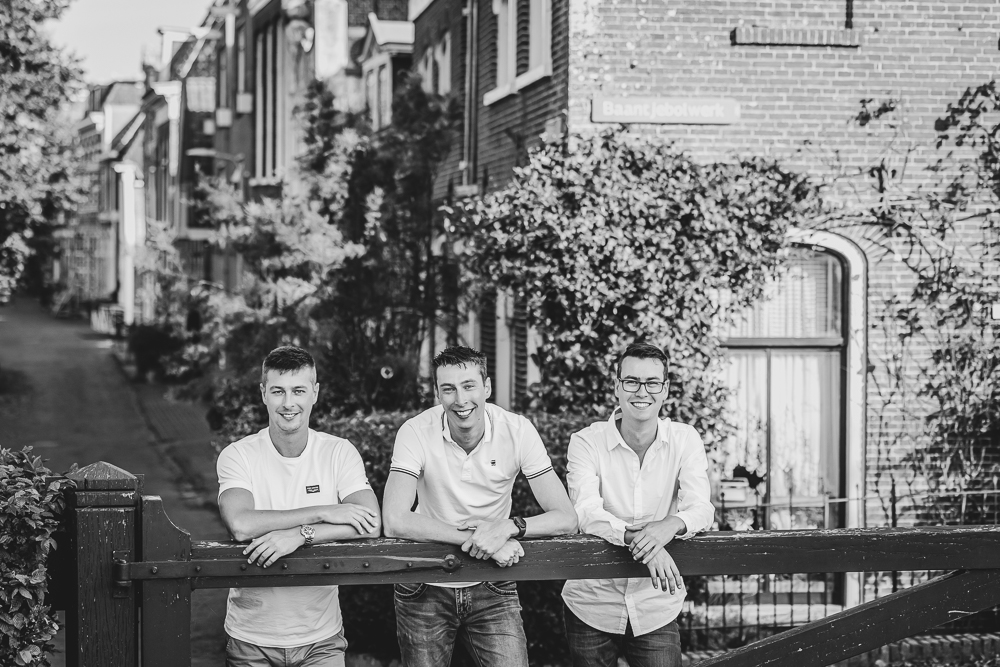 Fotoshoot Dokkum, Friesland. De drie broers staan bij het hekje met oud Dokkum op de achtergrond. Fotosessie door portretfotograaf Nickie Fotografie uit Dokkum.