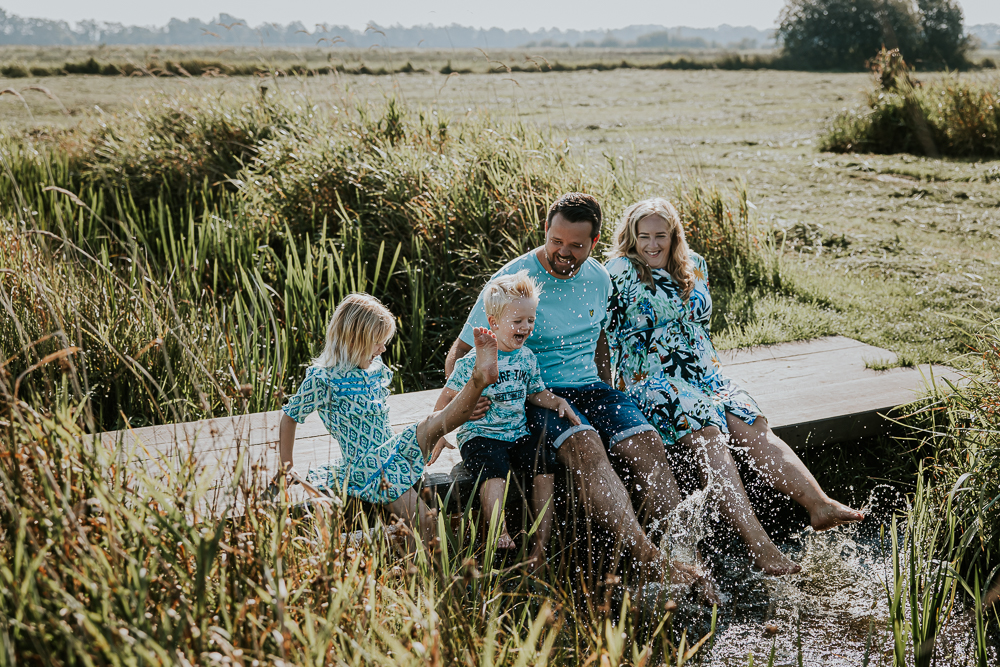 Lifestyle gezinsfotografie door fotograaf NIckie Fotografie uit Dokkum, Friesland. Het gezin zit op een houten loopbruggetje met de voeten in het water, lekker aan het spetten.