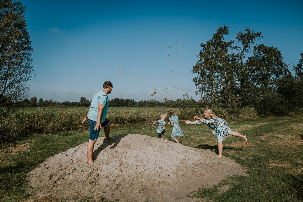 Het gezin gooit zand naar elkaar bij de zandbult. Fotoshoot Groningen door fotograaf NIckie Fotografie.