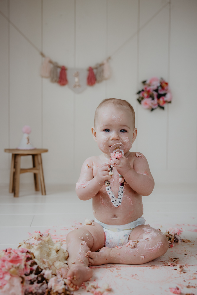 Cakesmash Friesland door fotograaf Nickie Fotografie. Meisje heeft heerlijk genoten van haar verjaardagstaart en geniet nu na met haar speen in haar mond.