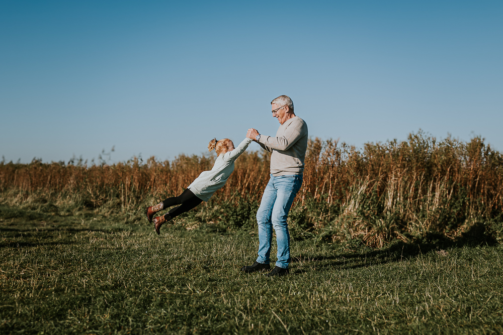 Opa zwaait zijn kleindochter in het rond. Familiereportage in het natuurgebied Lauwersmeer door fotograaf Nickie Fotografie uit Friesland.