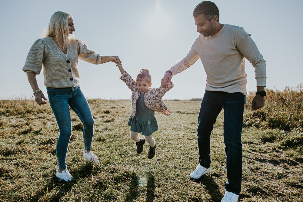 Fotograaf Friesland. De ouders laten hun peuterdochter zwaaien tussen hen in. Lifestyle gezinsshoot door Nickie Fotografie.