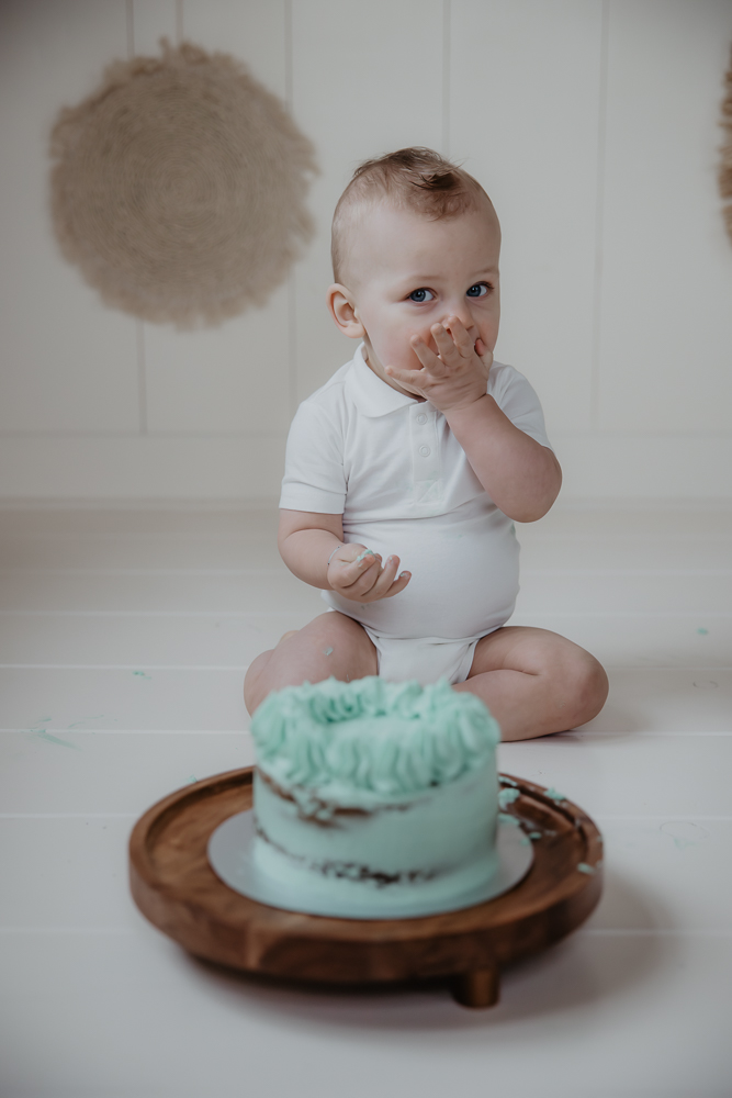 1 Jarige eet taart met zijn handen tijdens verjaardagshoot. Fotoshoot door fotograaf Nickie Fotografie.