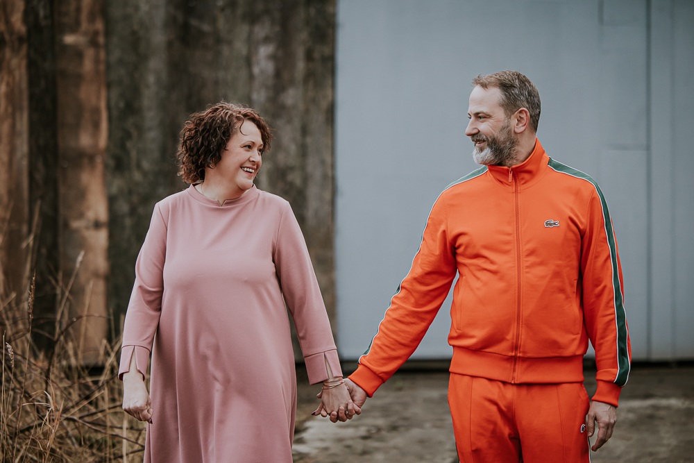 Wandelend portret van de ouders. Vader in oranje trainingspak en moeder en oudroze jurk. Industrieel gezinsshoot in door fotograaf Nickie Fotografie uit Dokkum, Friesland.