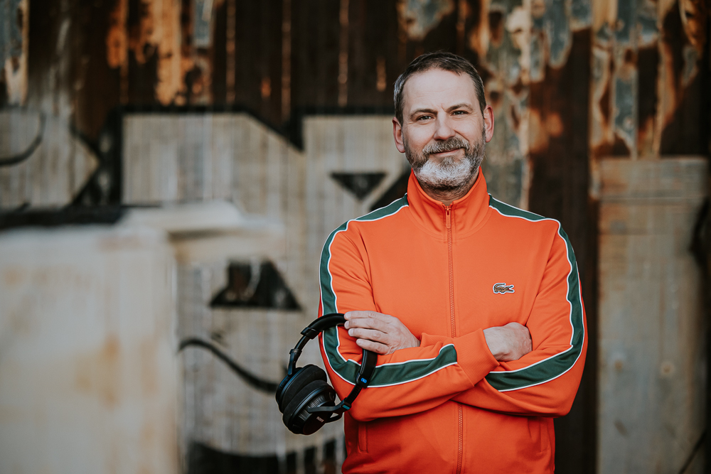 Fotograaf Friesland. Portret van muzikant in oranje trainingspak met koptelefoon in zijn hand voor een graffiti muur door Nickie Fotografie uit Dokkum.