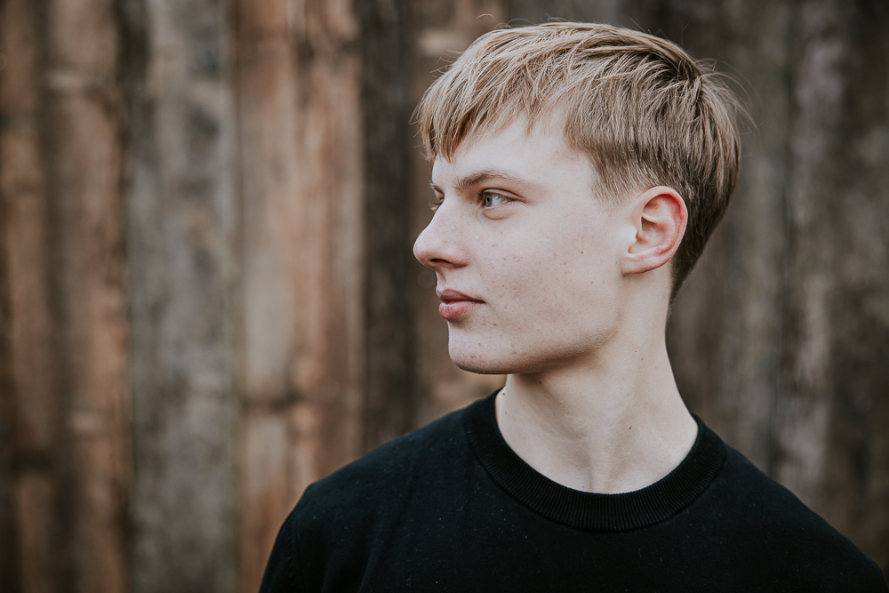 Portret van jonge man die opzij kijkt en voor een houten muur staat door fotograaf NIckie Fotografie uit Dokkum, Friesland.