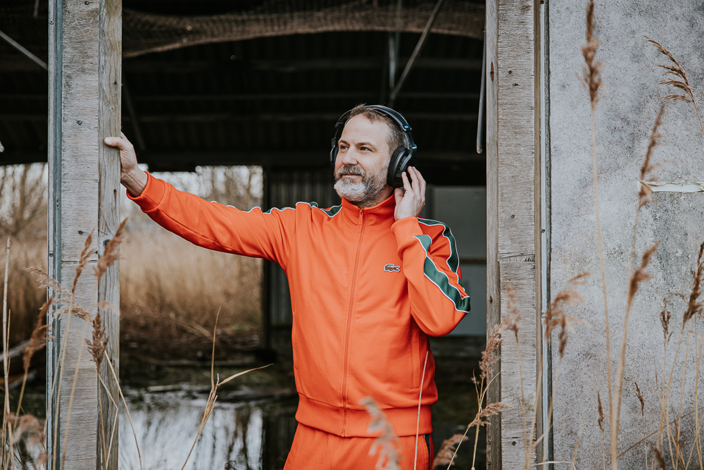 Portret met koptelefoon. Muzikant in oranje trainingspak luistert naar zijn muziek in verlaten gebouw. Fotoshoot Friesland door fotograaf Nickie Fotografie uit Dokkum.