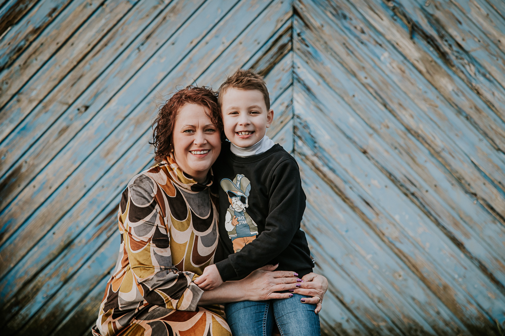 Fotograaf Friesland. Portret van moeder en zoon voor oude blauwe schuurdeur met diagonale balken. Gezinsreportage door fotograaf Nickie Fotografie uit Dokkum.