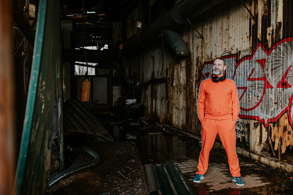 Portret van muzikant in oranje traininspak in urban omgeving door fotograaf Nickie Fotografie uit Dokkum, Friesland.