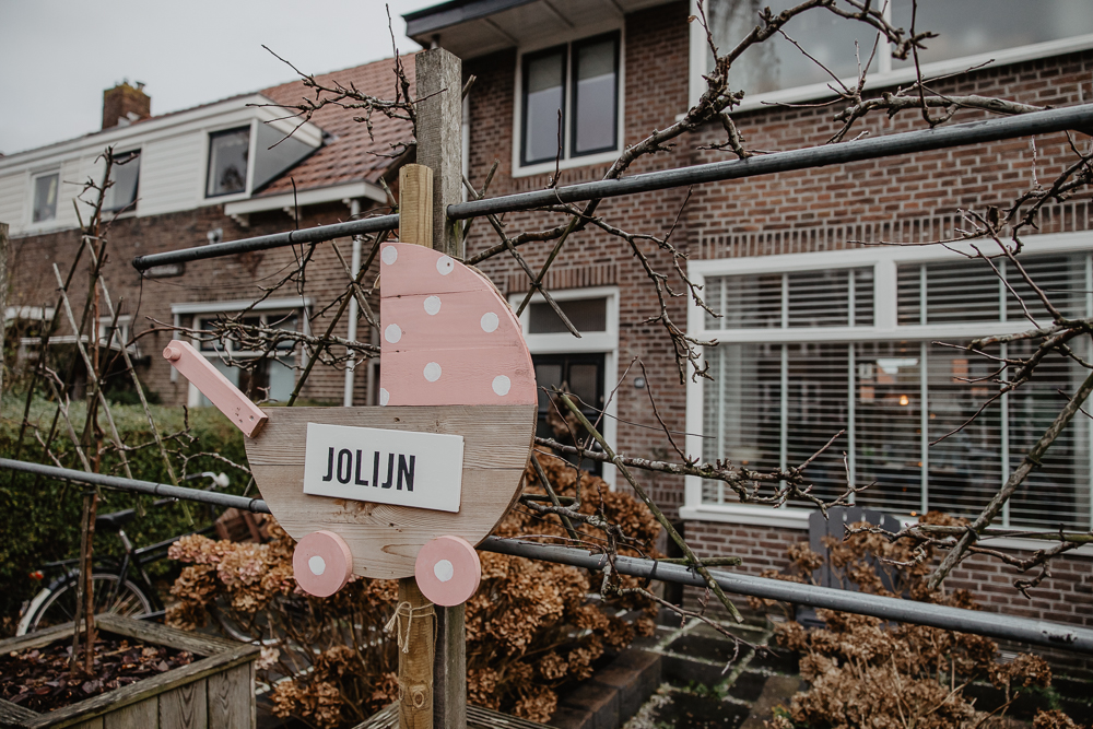 Babyreportage in Leeuwarden door fotograaf Nickie Fotografie uit Friesland. Grote roze houten kinderwagen op paal met naamplaat. 