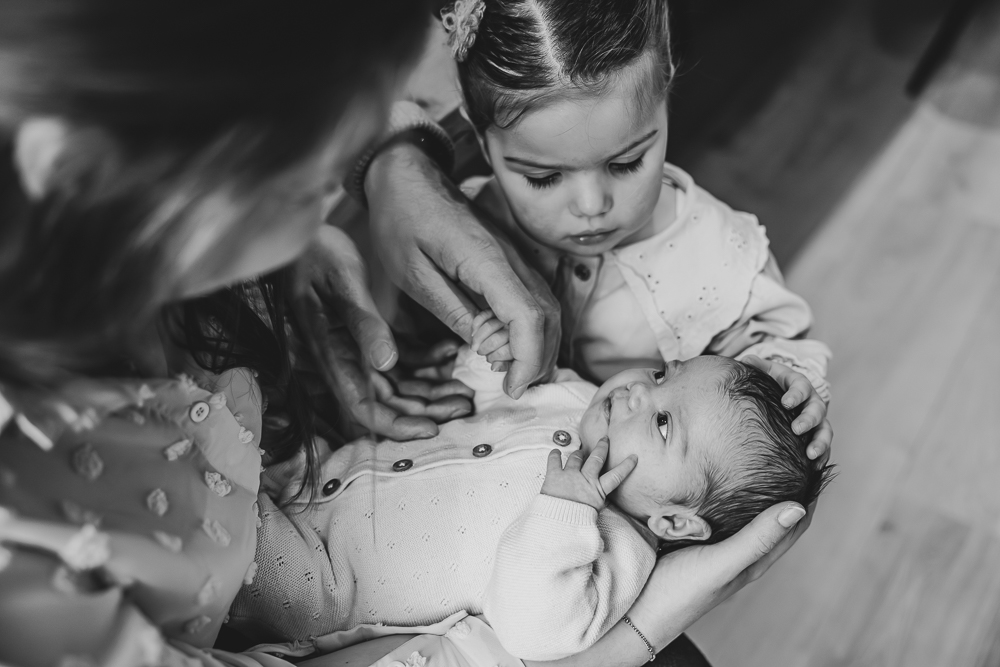 Gezinsreportage met baby in Leeuwarden, Friesland. Grote zus aait het hoofdje van haar pasgeboren zusje. Fotoshoot door fotograaf Nickie Fotografie.