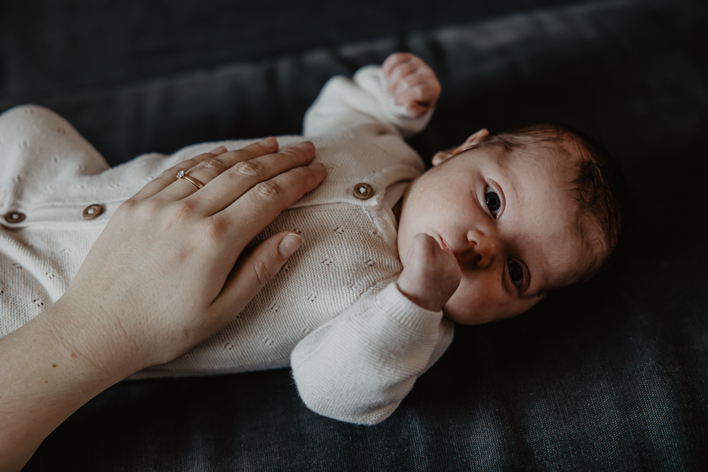 Babyshoot Friesland door fotograaf Nickie Fotografie. Portret van baby  liggend op de bank terwijl mama een hand op haar buikje heeft.