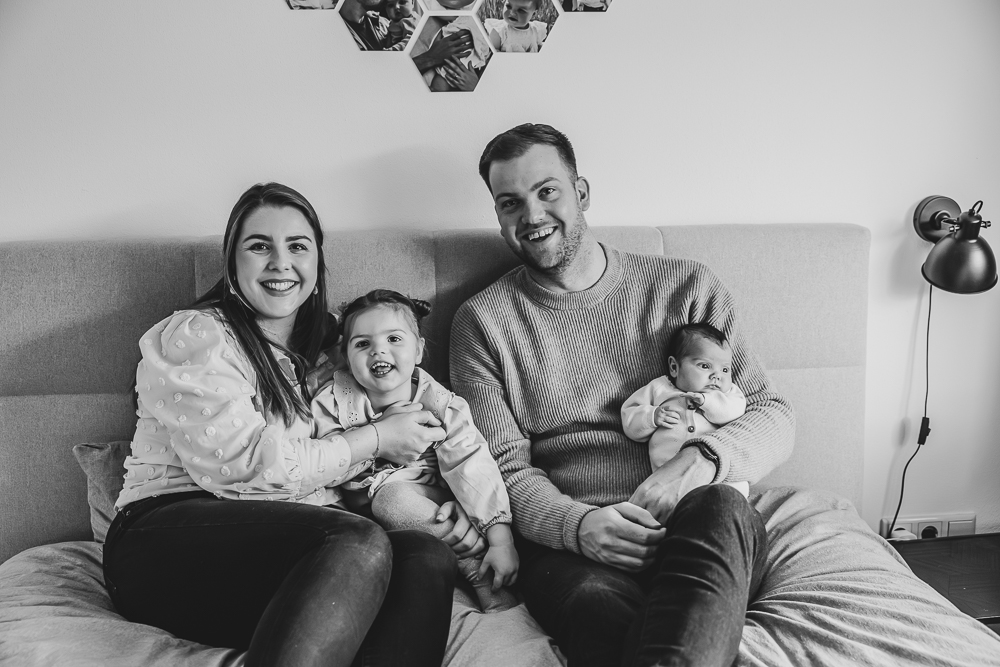 Fotograaf Friesland. Gezinsportret met baby thuis op het grote bed. Zwart-wit fotografie door fotograaf Nickie Fotografie uit Friesland.