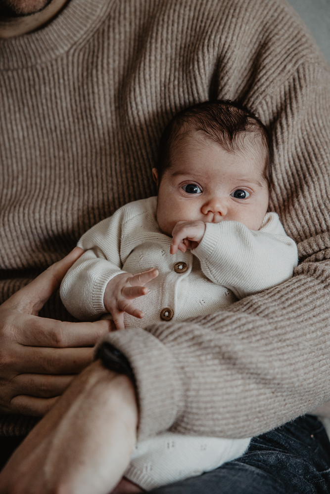 Babyreportage door fotograaf Nickie Fotografie. Vijf weken oude babymeisje zit lekker bij haar papa op schoot.