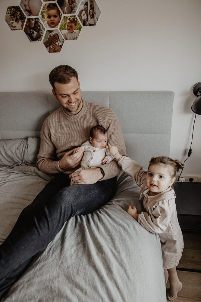 Newbornshoot Friesland door fotograaf Nickie Fotografie. Portret van vader met zijn twee dochters boven op het grote bed in de ouderlijke slaapkamer.