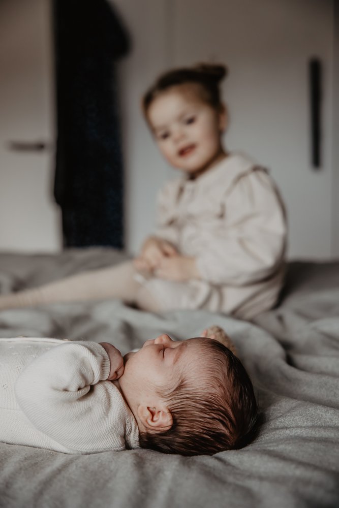 Babyshoot Leeuwarden. Portret van de twee schattige zusjes op het grote bed in de ouderlijk slaapkamer. Fotoreportage door fotograaf Nickie Fotografie uit Friesland.