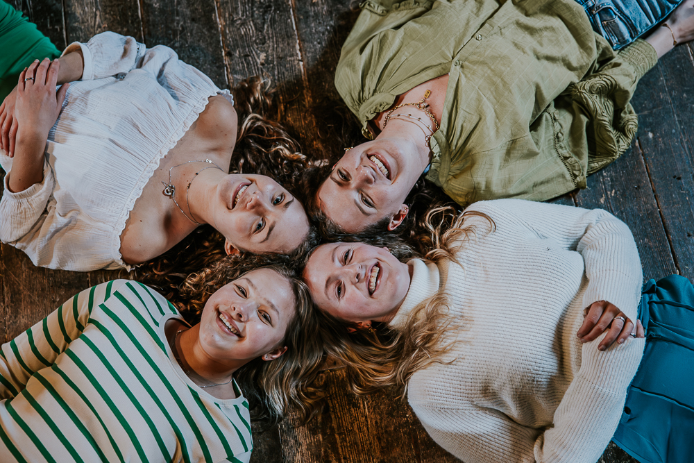 Vriendinnenshoot in molen. De vier vriendinnen liggen op de houten vloer van molen Zeldenrust met de hoofden tegen elkaar aan. Portret door fotograaf Nickie Fotografie uit Friesland.