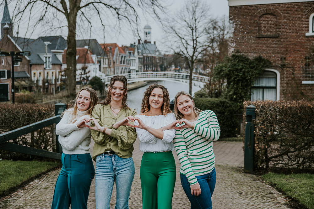 Fotoshoot Dokkum. Vriendinnenshoot in het pitoresque Dokkum. De vriendinnen maken hartjes met hun handen. Op de achtergrond zie je het oude Stadhuis. Fotoshoot door fotograaf Nickie Fotografie uit Friesland.