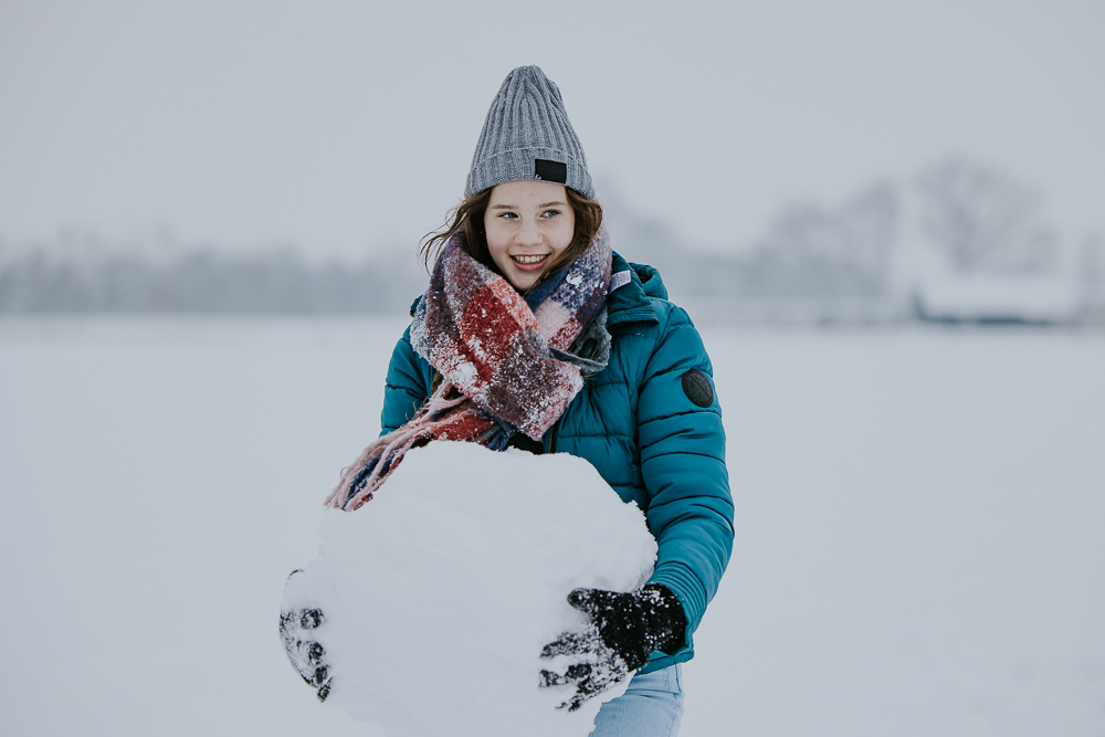 Winters portret. Meisje loopt met grote sneeuwbal. Fotoshoot door fotograaf NIckie Fotografie uit Dokkum, Friesland.