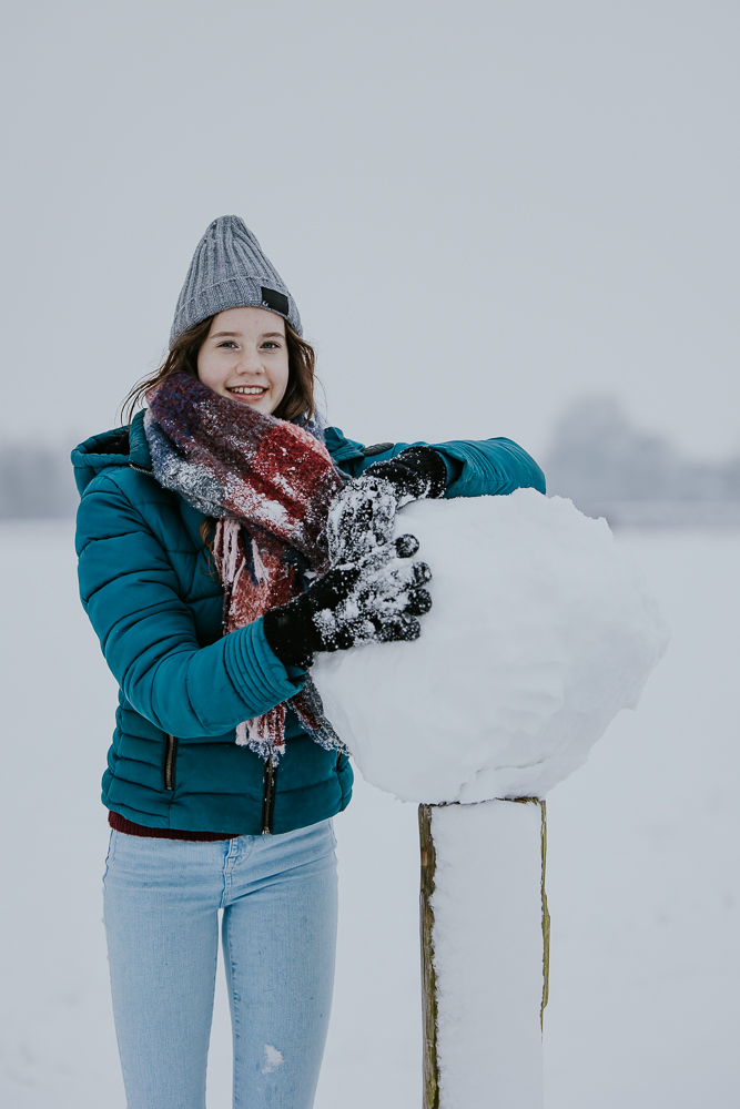 Winters portret. Meisje poseert met het grote sneeuwbal. Fotosessie door fotograaf Nickie Fotografie uit Dokkum, Friesland.