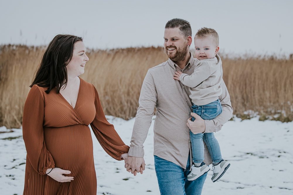 Zwangerschapsfotografie met partner en zoontje. Vrolijk wandelend portret tussen het wuivende riet door fotograaf NIckie Fotografie uit Dokkum, Friesland.