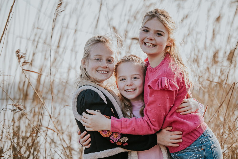 Gezinsshoot Lauwersoog door fotograaf Nickie Fotografie. Knuffelportret van de drie meiden voor het riet.