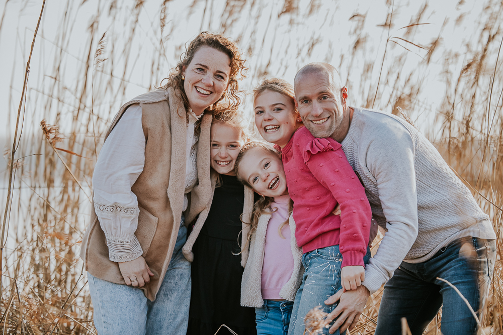 Gezinsshoot Lauwersoog. Gezellig knuffelportret van de ouders en hun kinderen voor een rietkraag. Gezinsreportage door fotograaf Nickie Fotografie.