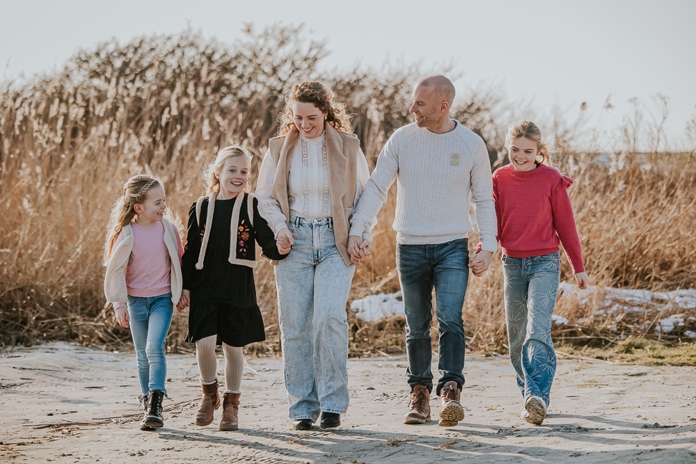 Fotograaf Lauwersoog. Gezinsreportage op het strandje door Nickie Fotografie. Het gezin loopt hand in hand over het strand.