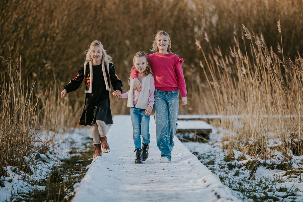 Gezinshoot Lauwersoog. De drie zussen wandelen gezellig over de besneeuwde vlonder bij het Lauwersmeergebied. Fotoreportage door fotograaf Nickie Fotografie.