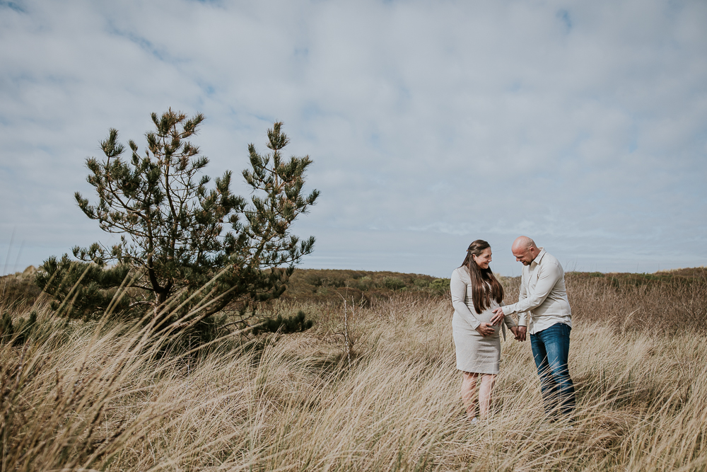 Fotoshoot Friesland. Een zwangerschapsreportage in de duinen door fotograaf Nickie Fotografie. Vader voelt liefdevol aan de bolle buik.