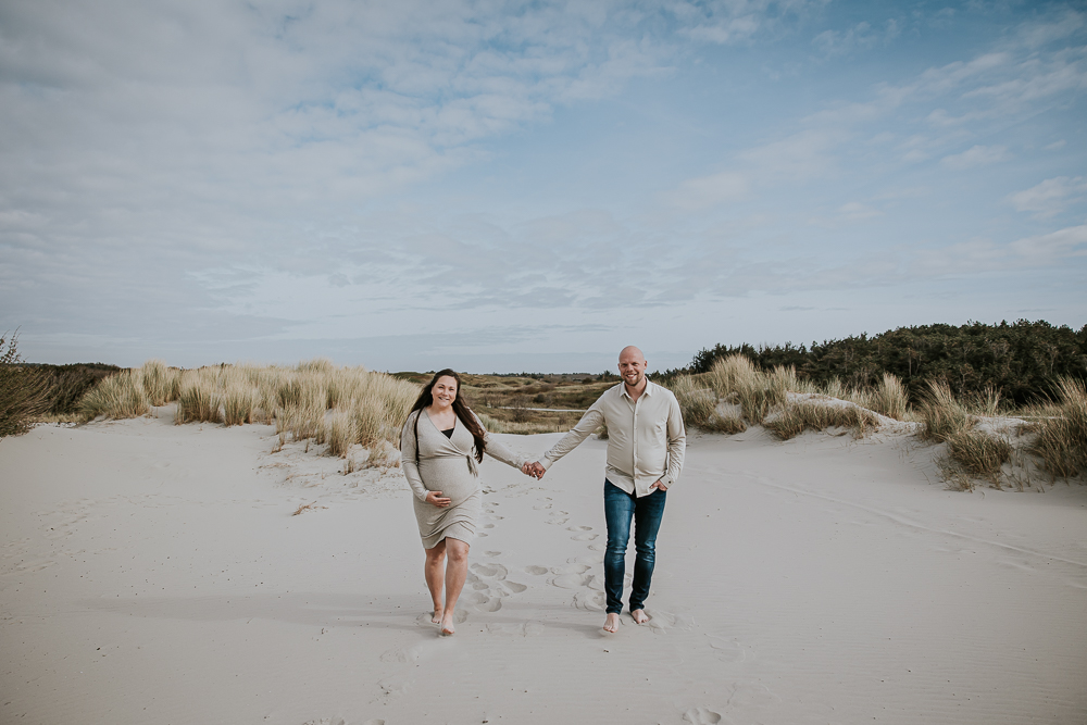 Zwangerschapsshoot Ameland door fotograaf Nickie Fotografie uit Friesland. De aanstaande ouders lopen hand in hand door de duinen.