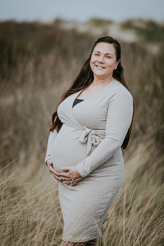 Bolle buik shoot in de duinen op Ameland. De aanstaande moeder draagt een zandkleurige jurk. Fotoshoot door fotograaf Nickie Fotografie.