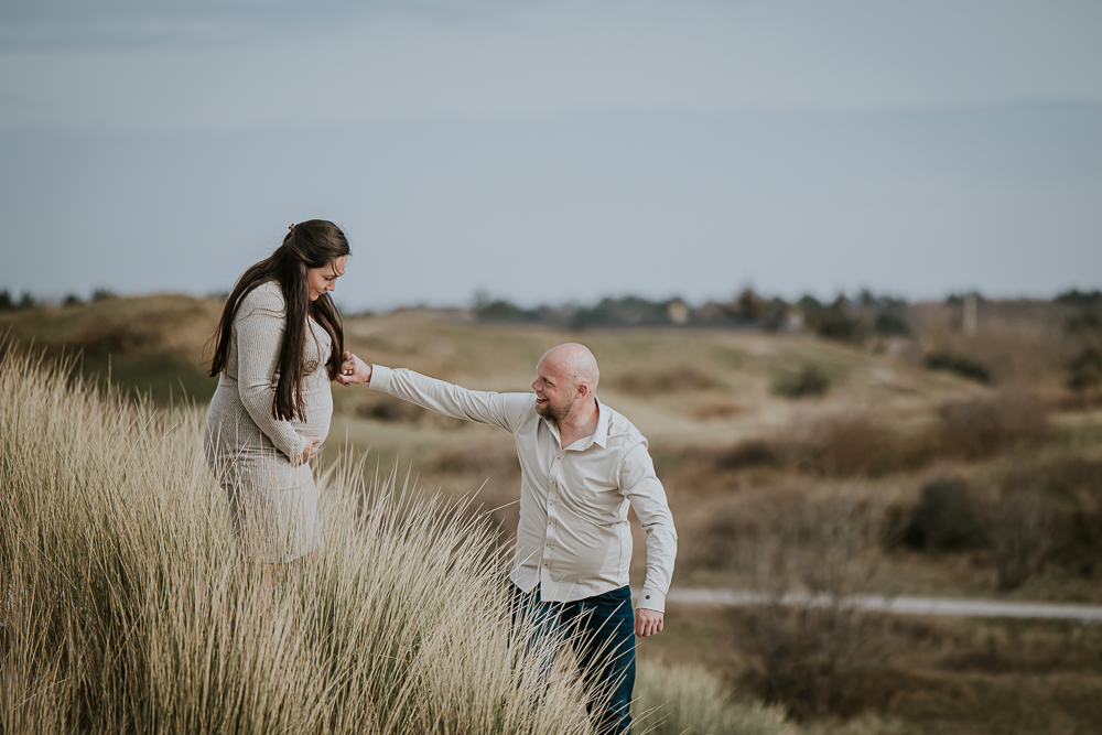 Zwangerschapsshoot met partner in de duinen van een Waddeneiland door fotograaf Nickie Fotografie uit Friesland. De aanstaande vader helpt de aanstaande moeder de duin af.