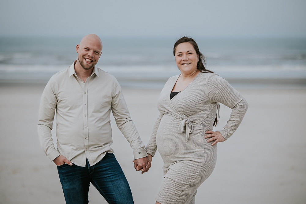 Bolle buik fotografie met partner. De aanstaande ouders staan hand in hand op het strand in zandkleurige kleding. Fotoreportage door fotograaf Nickie Fotografie.