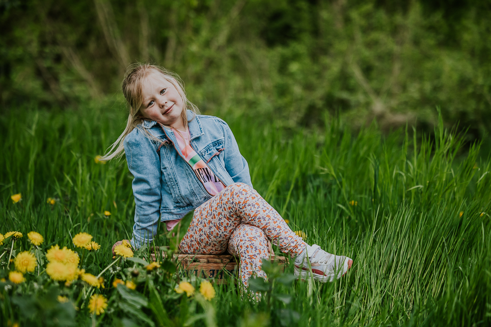 Kindershoot Dokkum. Meisje zit op houten kist in een grasveld met paardebloemen. Fotoreportage door fotograaf Nickie Fotografie uit Friesland.