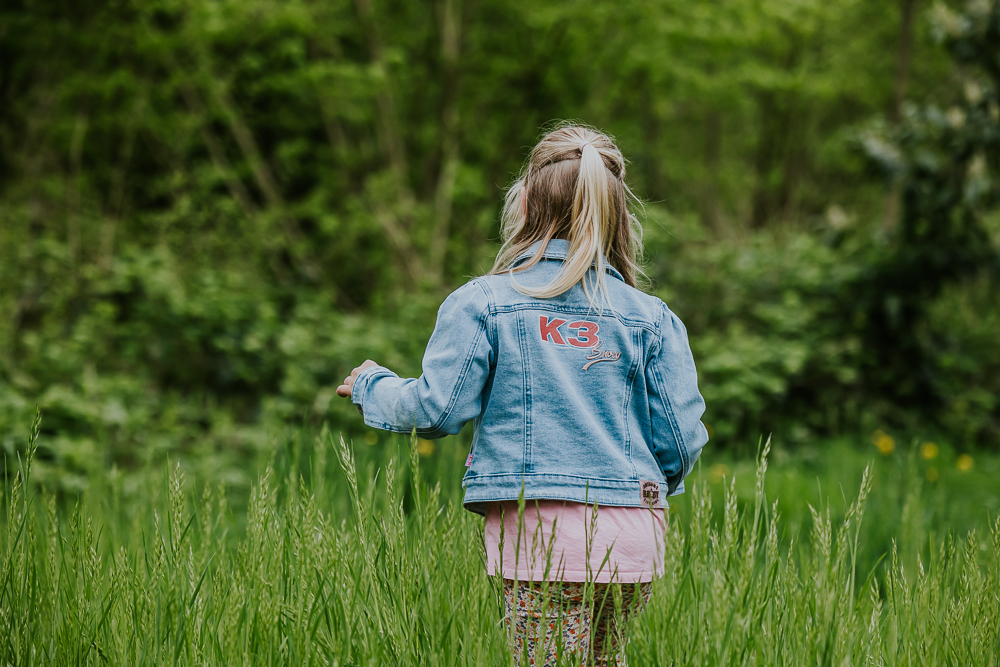Meisje met spijkerjasje van K3 loopt door het hoge gras. Fotograaf Friesland, Nickie Fotografie.