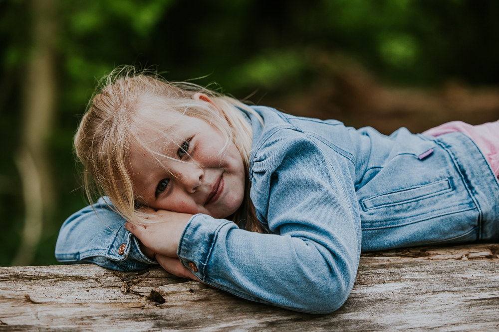Kinderportret. Meisje ligt op boomstam. Fotoshoot door fotograaf Nickie Fotografie uit Friesland.