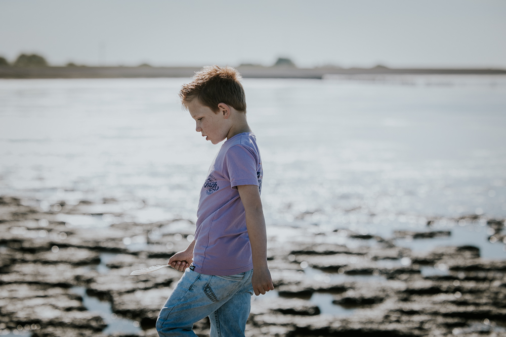 Fotoshoot Friesland. Jongetje loopt met een gevonden veer achter de zeedijk op het dammetje. Fotosessie door fotograaf Nickie Fotografie.