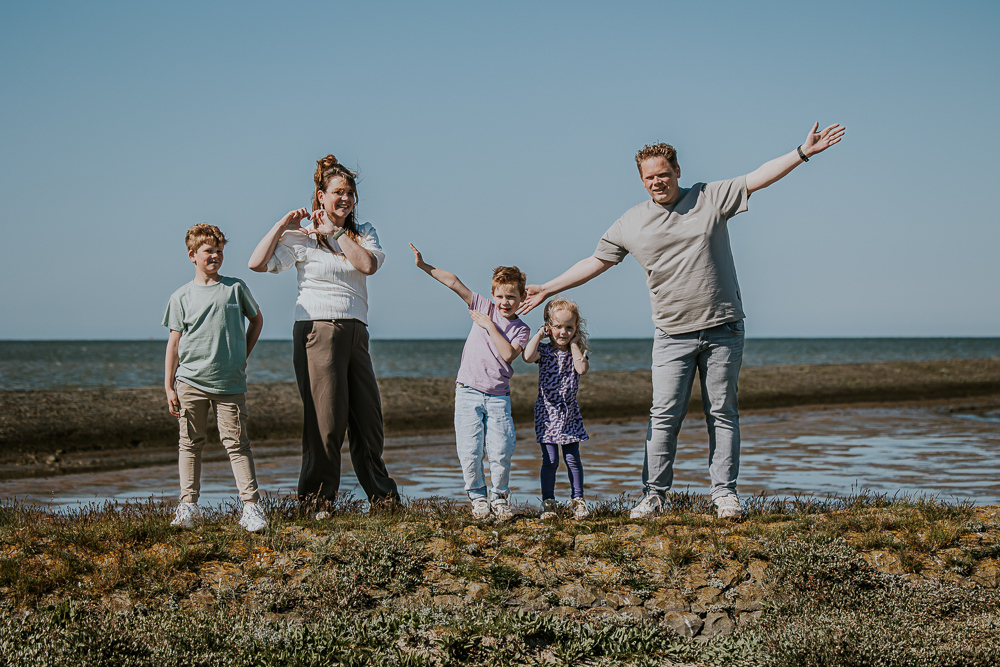 Speels gezinsportret bij het Wad. Iedereen doet een gekke houding. Fotoshoot Friesland door fotograaf Nickie Fotografie.