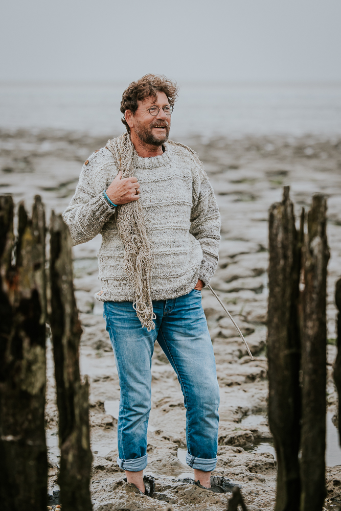 Fotograaf Friesland. Model staat in visserstrui met blote voeten in het Wad bij de paaltjes van Moddergat. Fotoshoot door Nickie Fotografie.