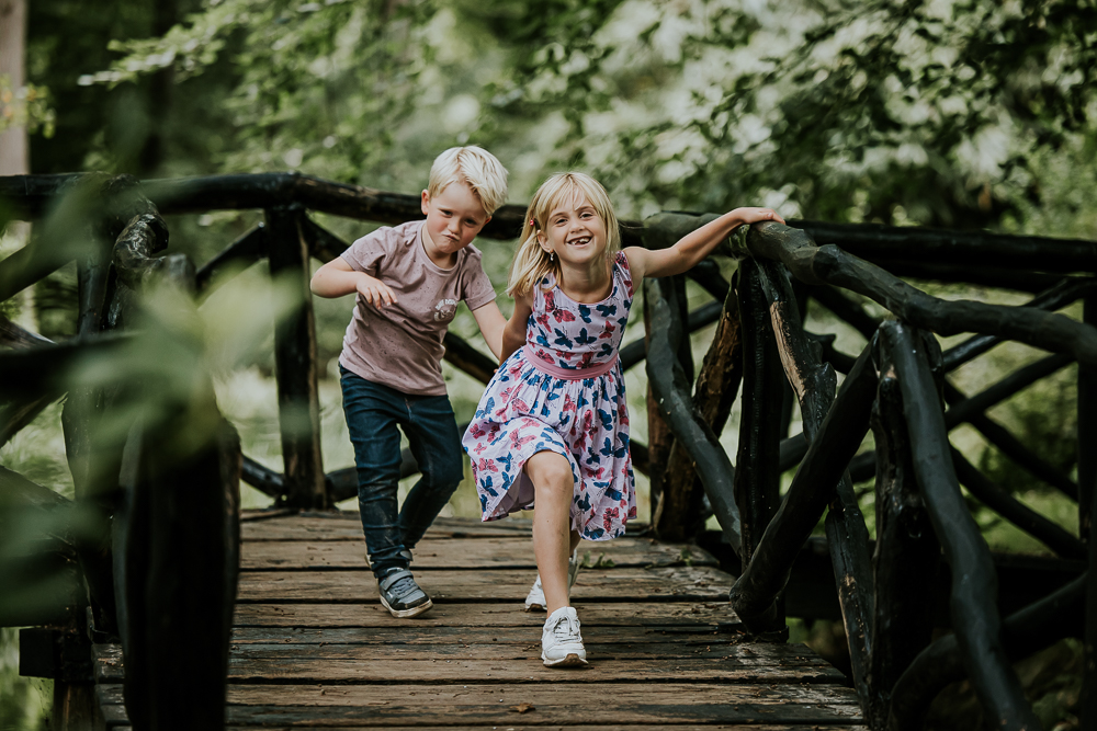 Fotoshoot park Vijversburg. De kinderen doen een gekke loopje op een houten bruggetje. Gezinsfotografie door fotograaf Nickie Fotografie.