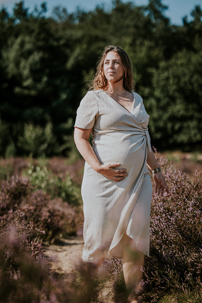 Zwangerschapsfotografie Bakkeveen. Portret van de aanstaande moeder lopend in de hei. Bolle buikshoot door zwangerschapsfotograaf Nickie Fotografie uit Friesland.