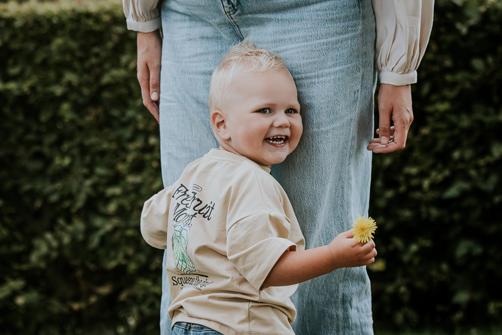 Fotograaf Friesland. Portret van lachend jongetje die de benen van zijn moeder vasthoudt en in zijn andere hand een bloemetje heeft.
Fotoshoot door Nickie Fotografie.











